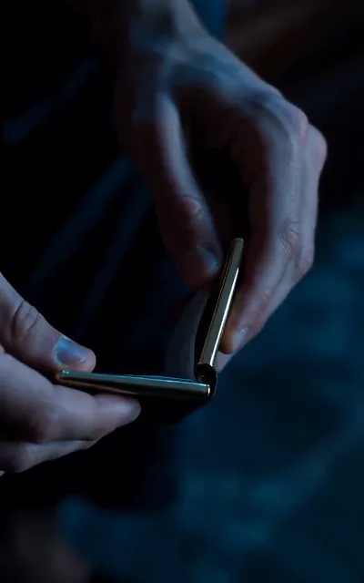 Cold-blue close-up of hands turning a small metal clasp — the calm before the cliffhanger